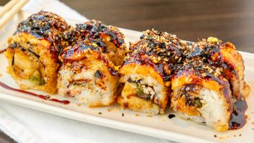 Close-up of sushi rolls drizzled with sauce and sprinkled with sesame seeds.