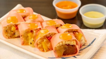 Pink sushi rolls with fruit filling and dipping sauces on the side.