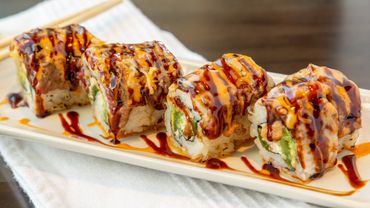 Close-up of sushi rolls drizzled with sauces on a white plate.