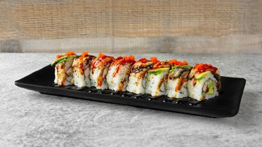 A neatly arranged sushi roll garnished with sauce and roe on a black platter.