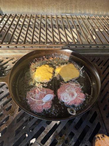 Cheeseburgers and patties cooking in a cast iron pan with onions.