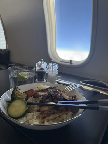 Meal with rice and vegetables served on an airplane tray table by the window.
