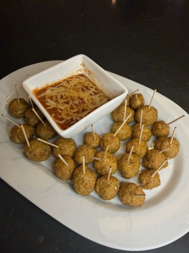 Plate of meatballs with toothpicks and a bowl of marinara sauce topped with cheese.