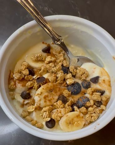 Bowl of yogurt with banana slices, blueberries, granola, chocolate chips, and cinnamon.