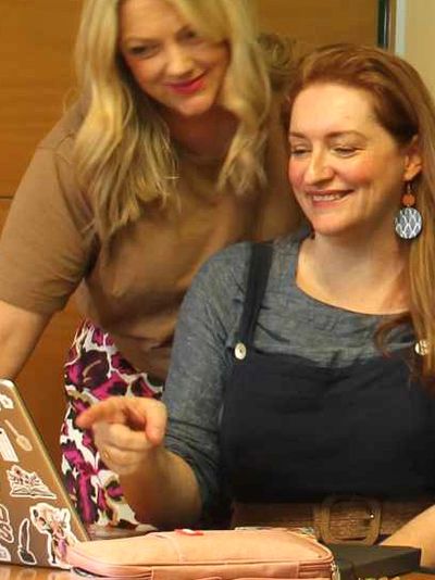 Two women smiling and looking at a laptop together.