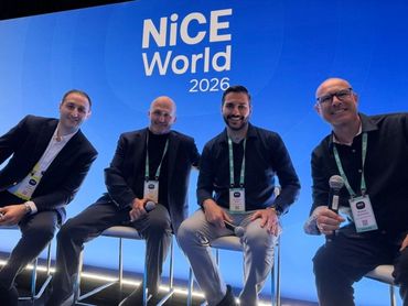 Four men sitting on stools at NiCE World 2026 event, smiling and holding microphones.