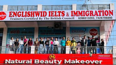 Group of people standing on a balcony under Englishwid IELTS & Immigration sign.