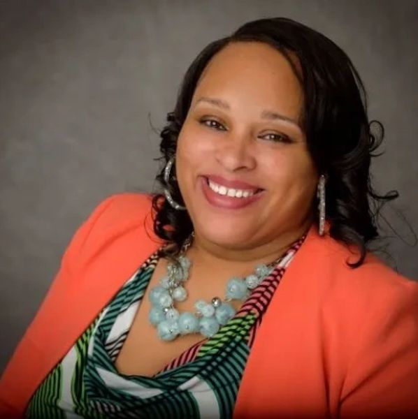 Smiling woman in colorful outfit with necklace and earrings.