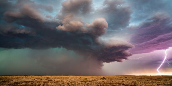 A dramatic storm cloud with lightning over a dry field.