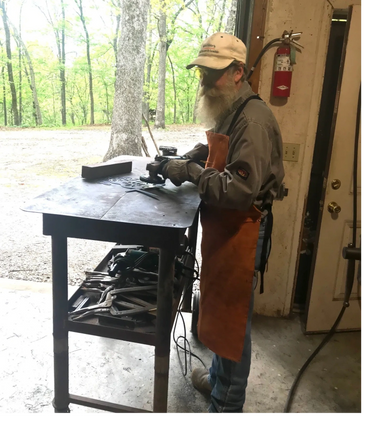 Older man with a beard working on metal art in a workshop.
