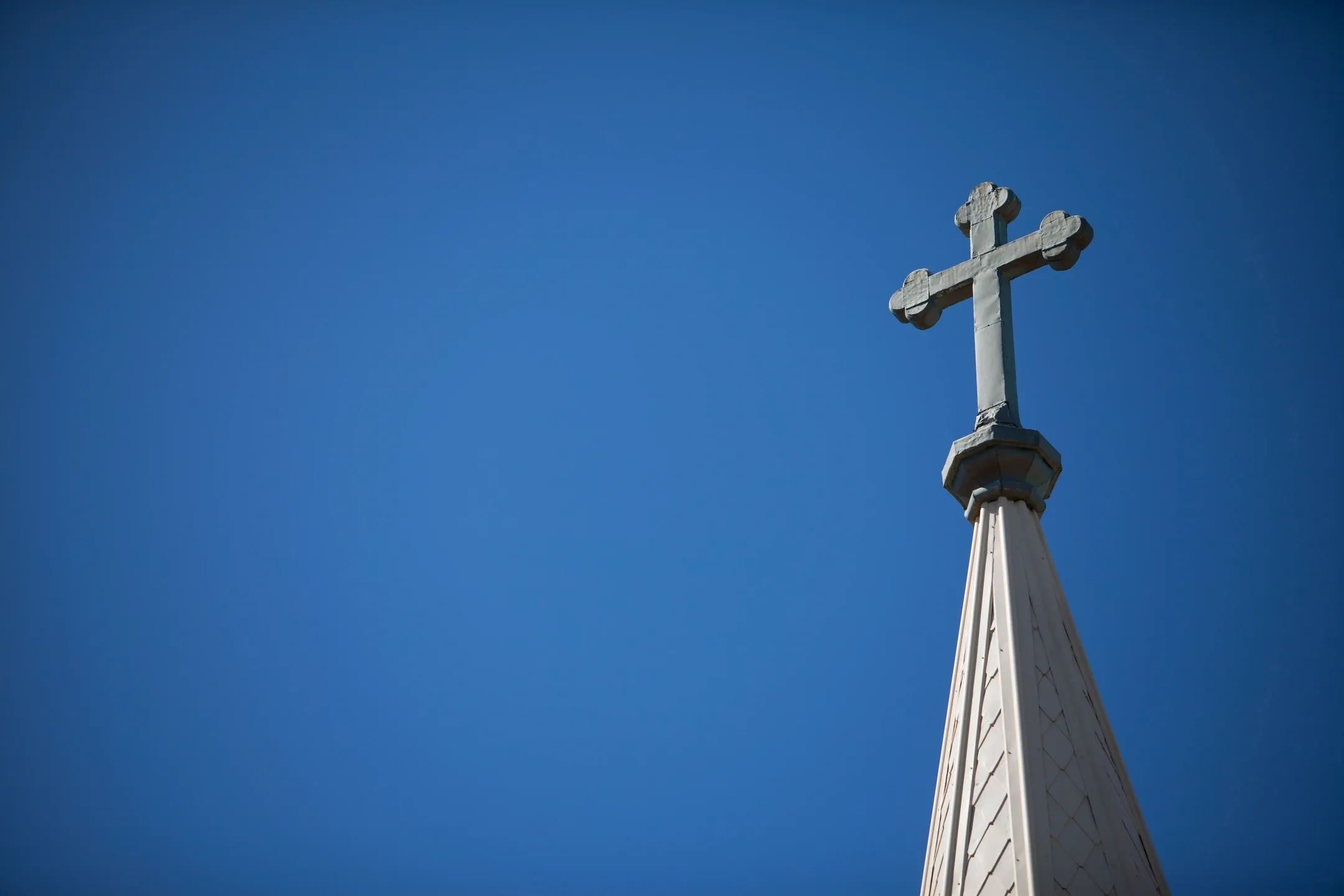 A church steeple with a cross on top against a clear blue sky
