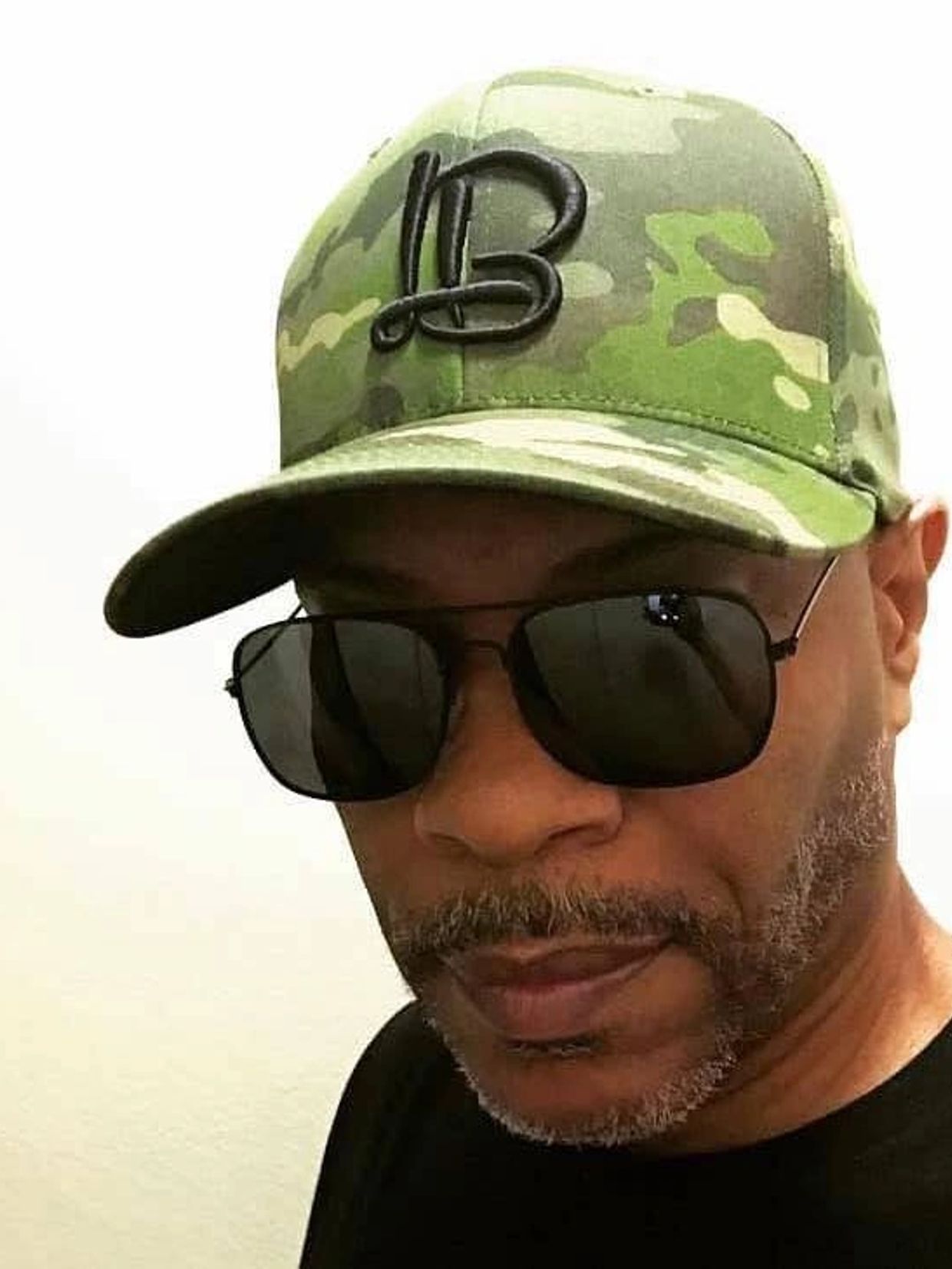 Man wearing camouflage cap and black sunglasses.