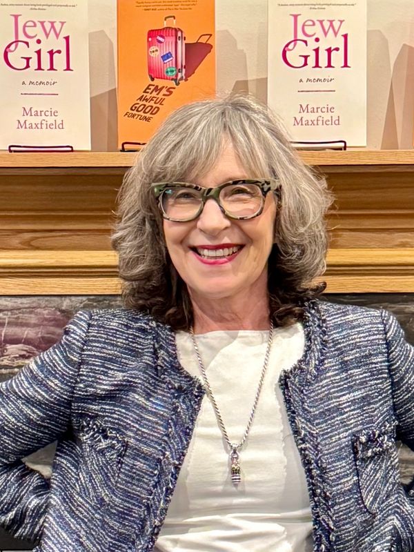 Smiling woman with glasses and gray hair, sitting in front of books.