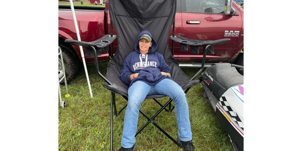 Person relaxing on an oversized black chair outdoors beside a red truck.