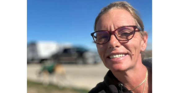 Smiling woman with glasses outdoors on a sunny day.