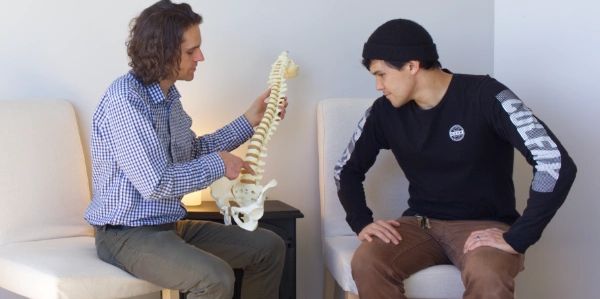 Dr. Leins holding up a model of a spine while talking with a patient.