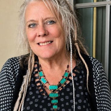 Woman with blonde dreadlocks wearing turquoise jewelry and a patterned top.