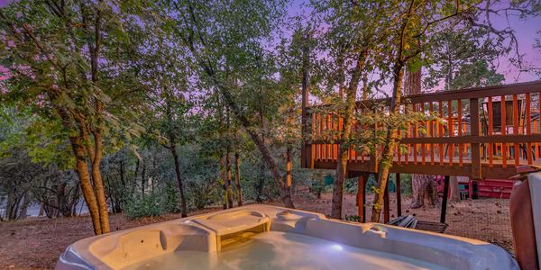 Hot tub surrounded by trees and a wooden deck at sunset.