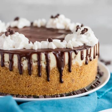 A creamy cheesecake with chocolate ganache and whipped cream on a crumb crust.