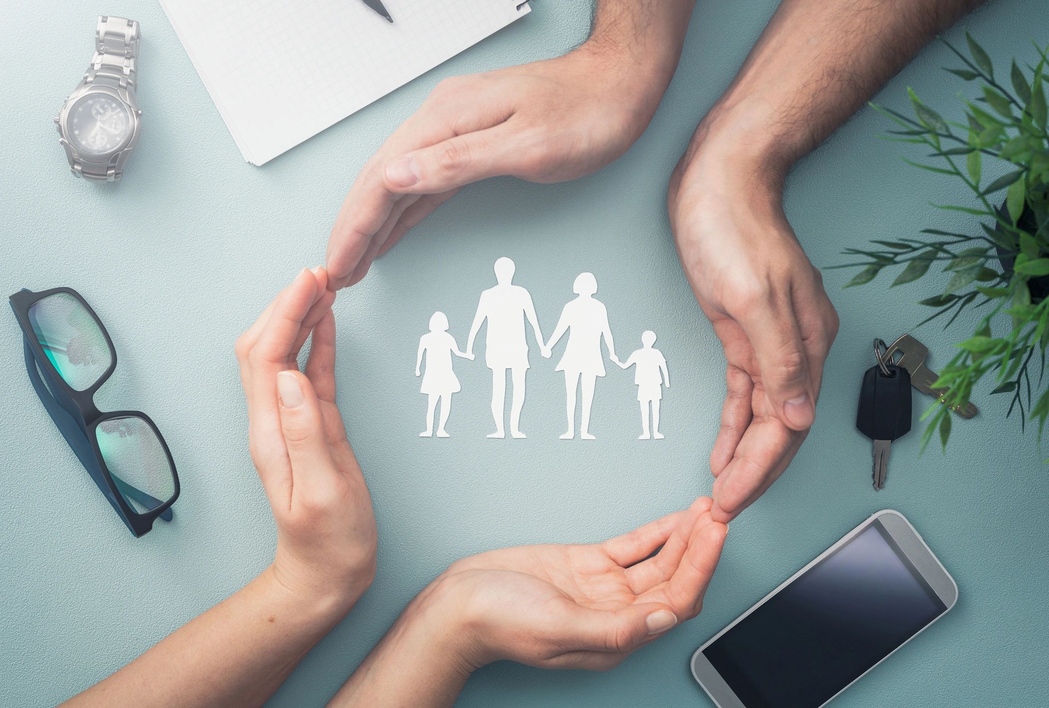 Four hands form a circle around a paper cutout of a family, symbolizing protection