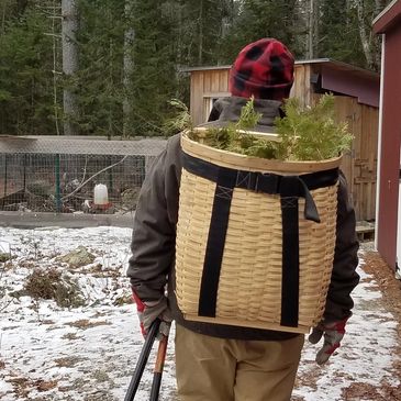 Bas Rouge Farm & Forge male farmer walking toward the woods with pack basket on his back in winter.