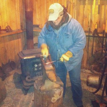 Bas Rouge Farm & Forge Female farmer in a blacksmithing forge using a hammer on an anvil.