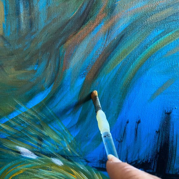 Close-up of a paintbrush adding details to a vibrant blue and green painting.