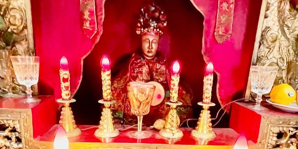 An ornate altar with a statue, candles, and offerings in a red setting.