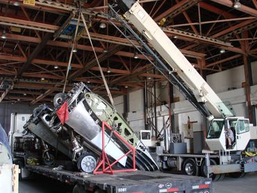A crane lifts a partially assembled aircraft from a truck