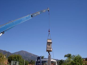 A crane lifts a large birdhouse against a clear blue sky