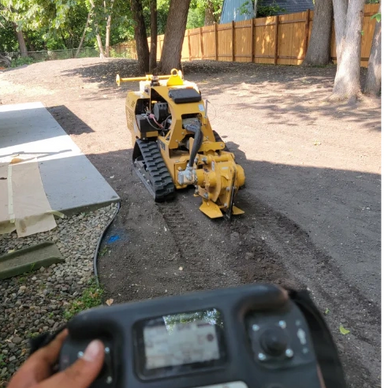 Remote-controlled yellow construction machine digging soil in a backyard.
