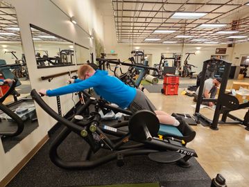 Person stretching forward on a fitness machine in a gym.