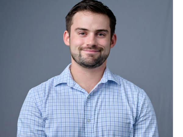 Smiling man in a checkered shirt against a gray backdrop.