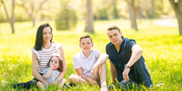 A family of four sitting on grass in a sunny park.