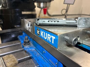 A metal vise labeled Kurt holding a handgun slide in a workshop.