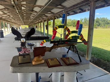 A rifle, trophies, and wind flags on a concrete table at an outdoor shooting range.