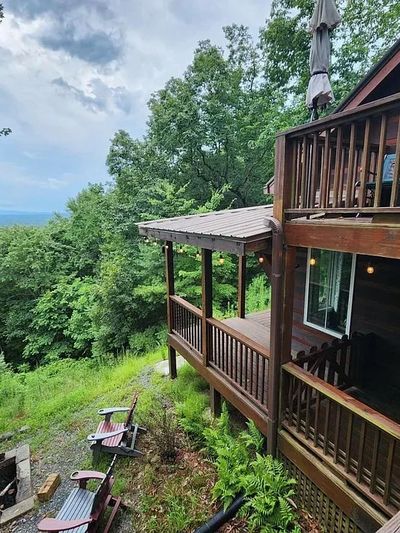 Wooden cabin deck overlooking lush green forest and distant hills.