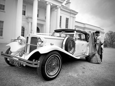 bride and groom leaning on vintage wedding car, mansion in background