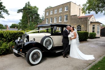 bride and groom kissing in front of a vintage wedding car, registry office in background