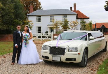 bride and groom standing outside a farmhouse with a limousine