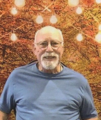 Smiling elderly man in glasses and blue shirt with warm autumn background and string lights.