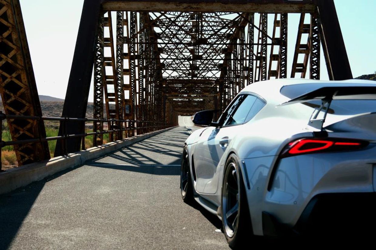 A sleek silver sports car on a metal bridge with intricate framework.