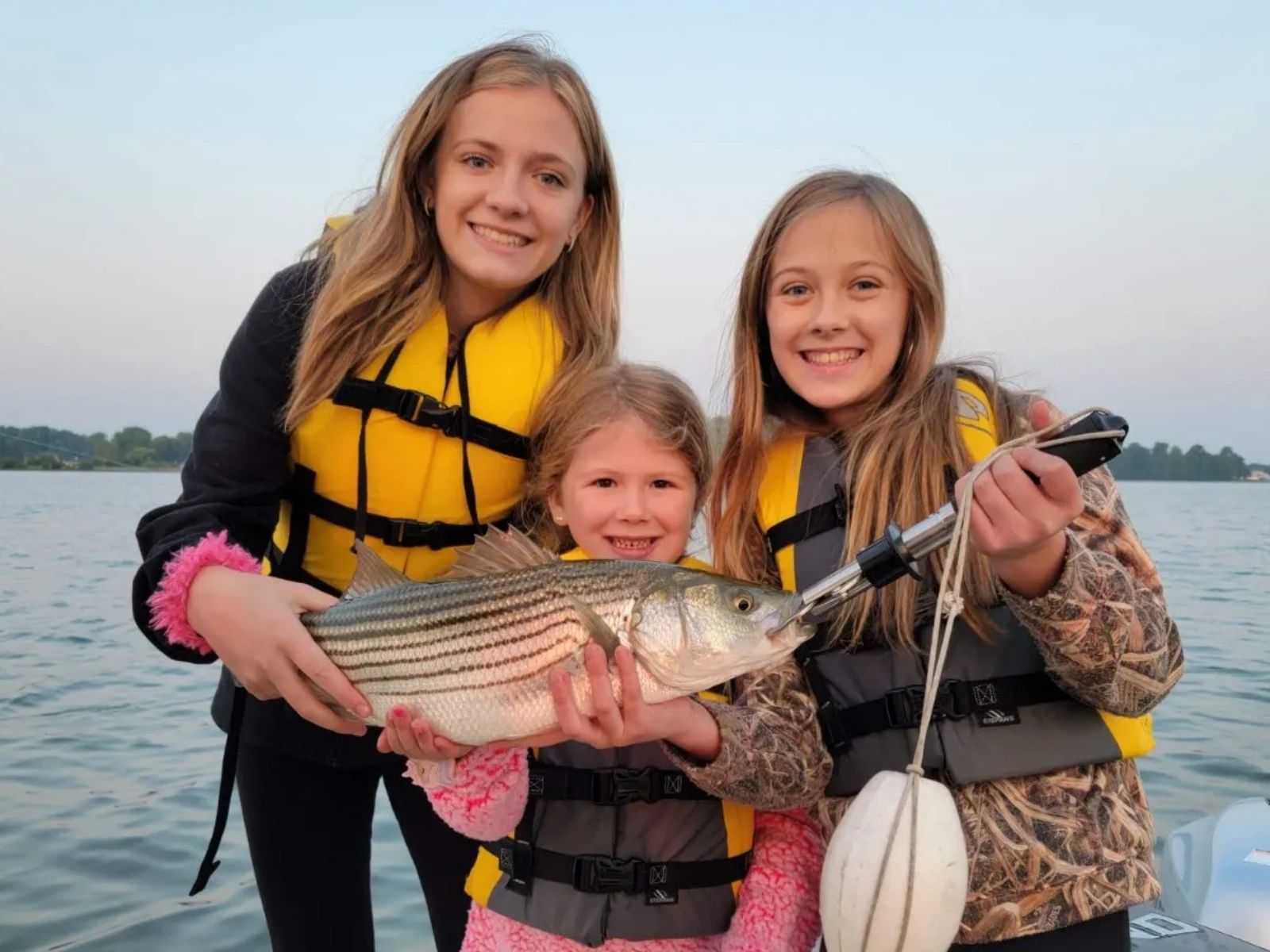 Three girls on a boat holding a striped bass they caught at Smith Mountain Lake, Virginia