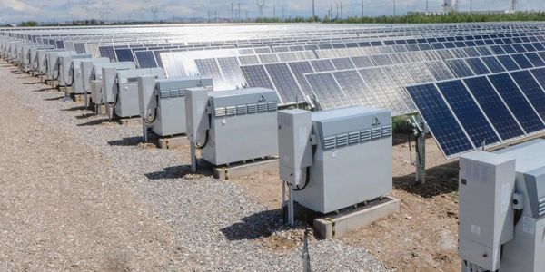 Rows of solar panels in a solar farm with electrical boxes.