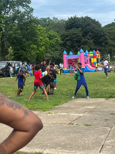 Kids playing and running near a bounce house at a park event.