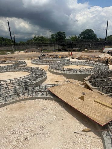 Curved concrete foundation with metal reinforcement at a construction site.