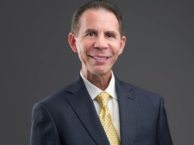 Professional man in a suit with a yellow tie smiling against a gray background.