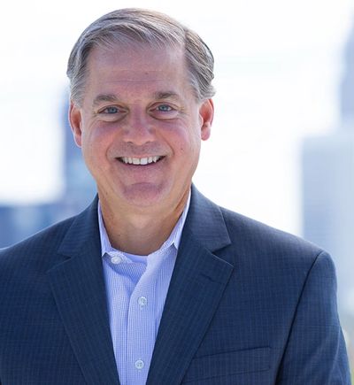 Smiling man in a suit with a cityscape background.