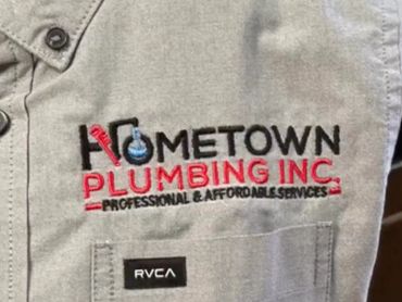 Close up of Hometown Plumbing embroidery logo on gray button-up shirt