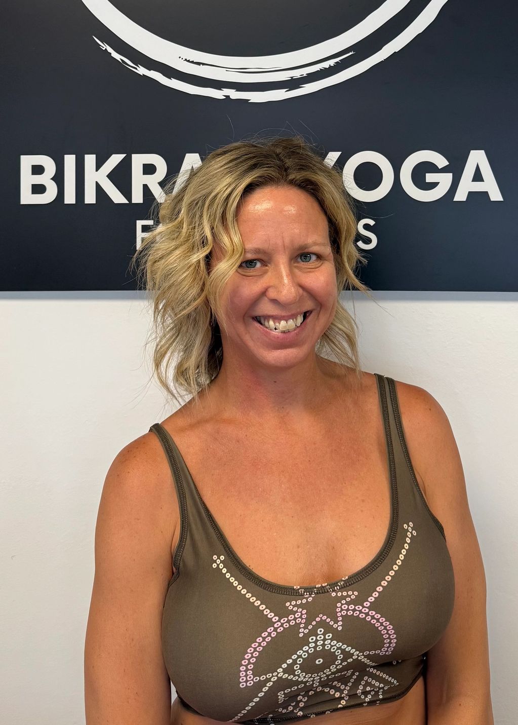 Smiling woman in yoga attire in front of a Bikram Yoga sign.